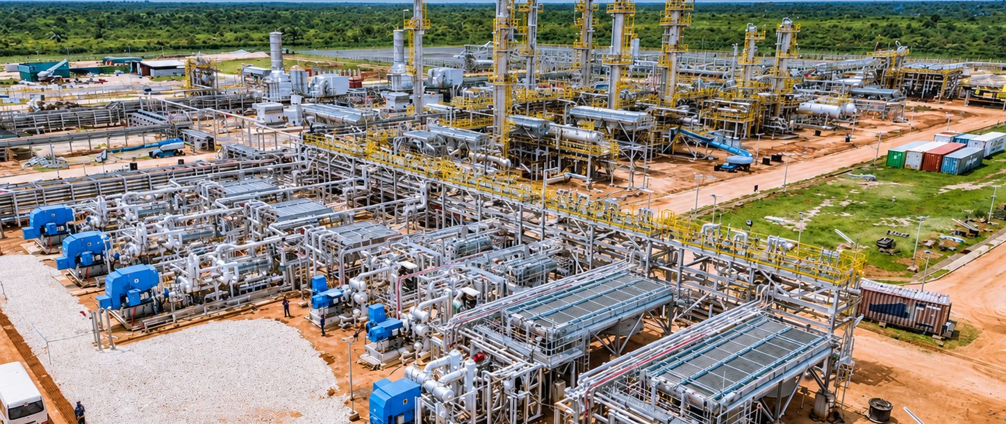 Aerial view of a gas processing plant under construction with compressor skids and process columns amid green bushland